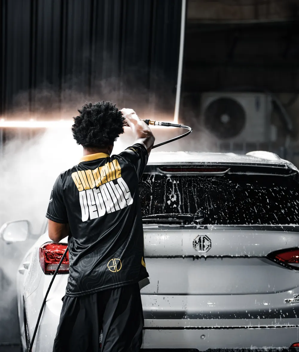 Supreme Details detailer in team jersey pressure-washing a silver MG SUV in the San Juan studio
