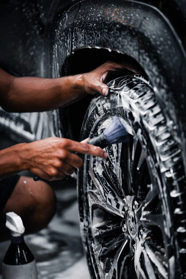 Detailer scrubbing a foamed alloy wheel and tyre with a soft brush